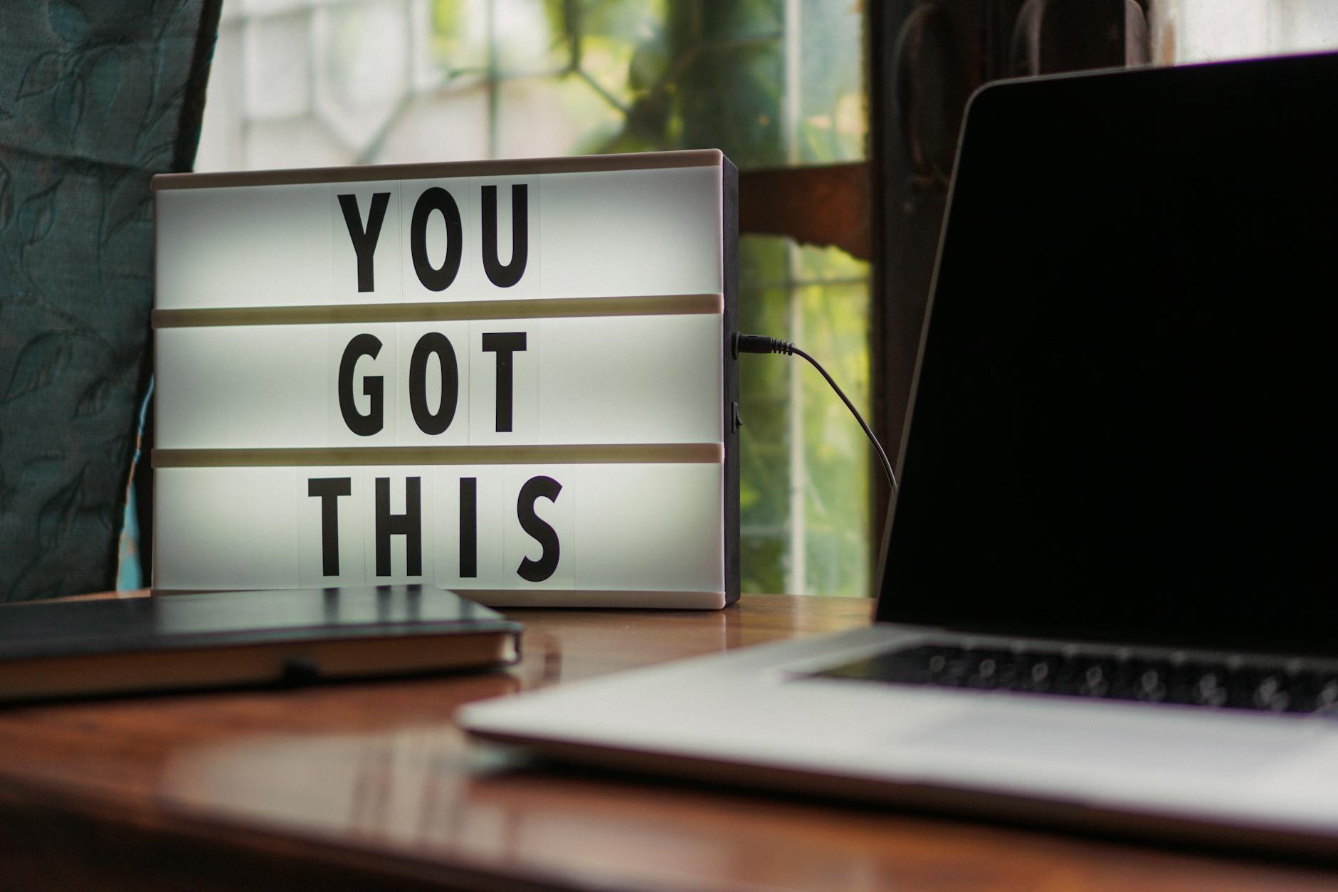 Een bureau met een laptop en een bord met de tekst "You got this"